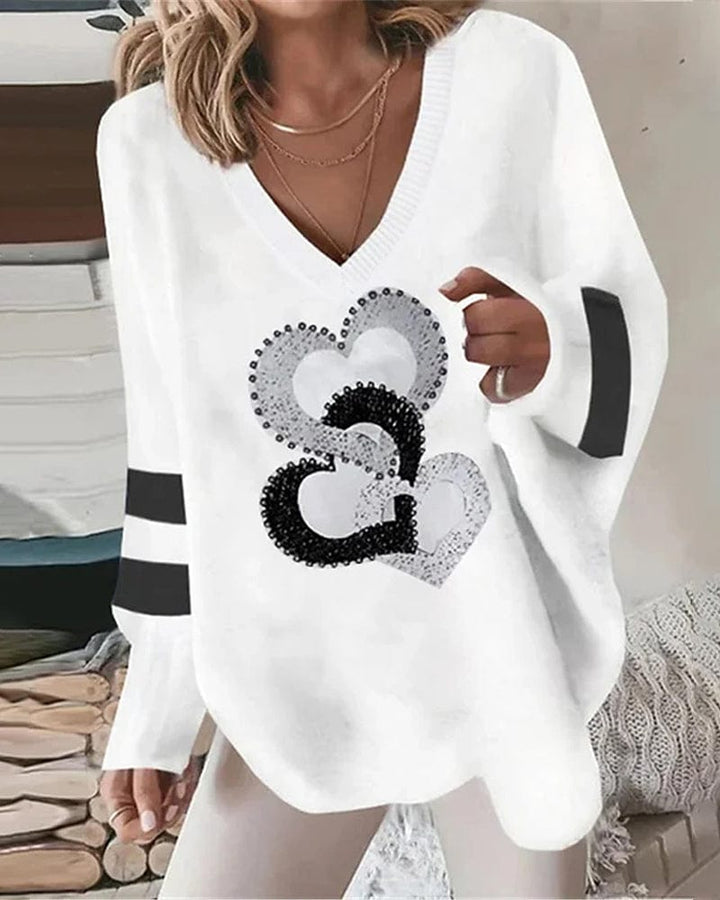 Front view of a model wearing a white loose fit long sleeve V-neck shirt with black and white heart print