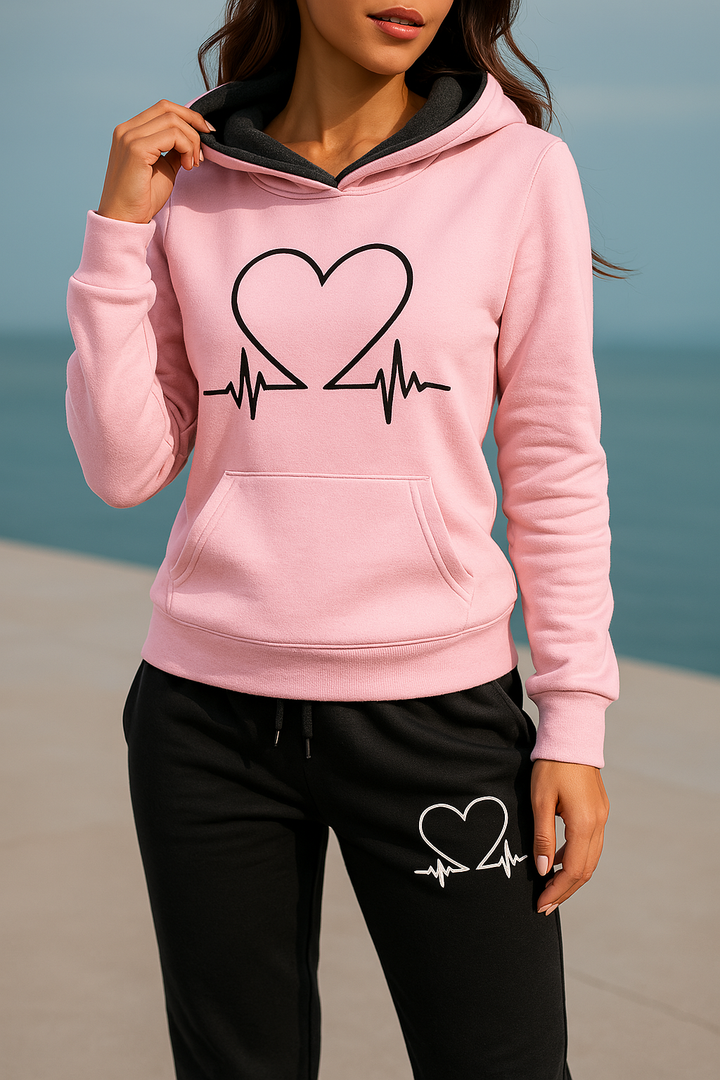 Front view, model wearing a pink Heartbeat Tracksuit sweatshirt with a black heart graphic and black joggers