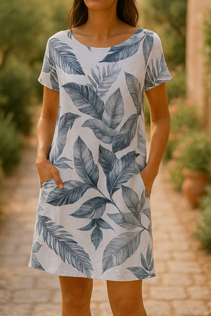 Front view of a model in an elegant summer dress with a blue botanical print, hands in pockets