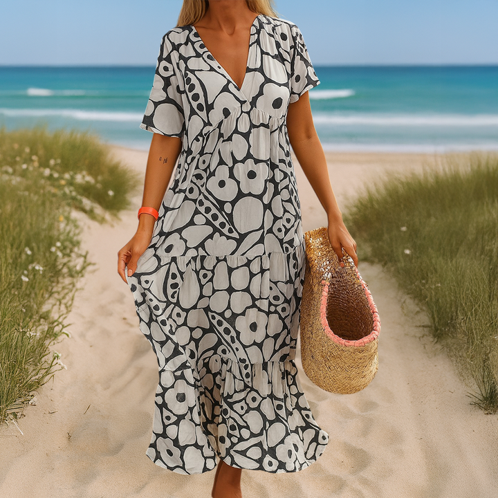 Front view, model wearing a black and white patterned summer dress on a sandy path with ocean in background