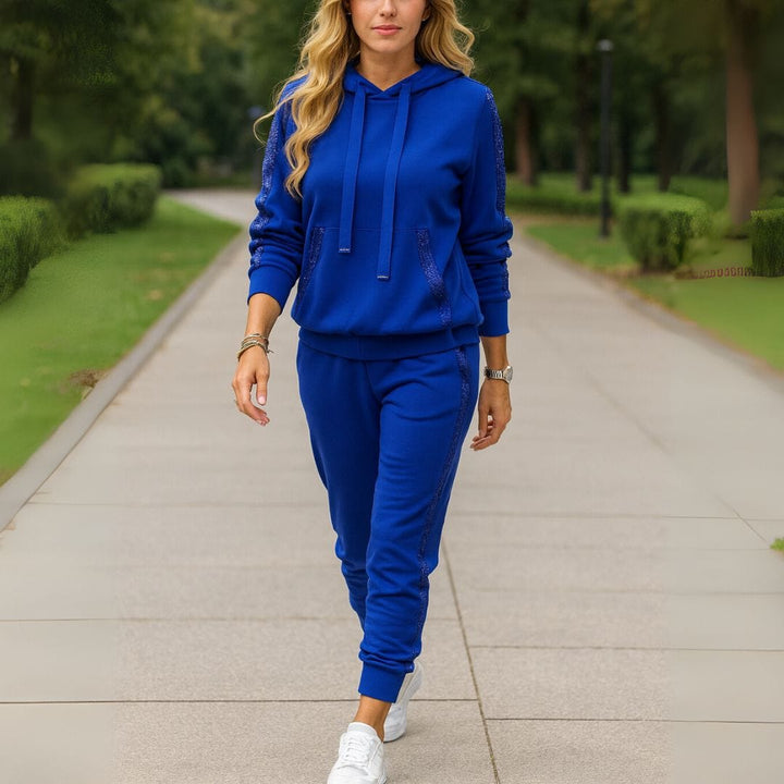 Front view of a woman walking in a blue sequin patchwork hoodie tracksuit set on a paved path