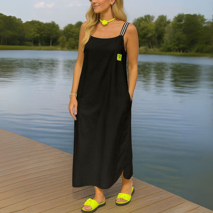 Three quarter view of a model in a black U-collar loose pullover ankle dress with pockets, standing by a lake