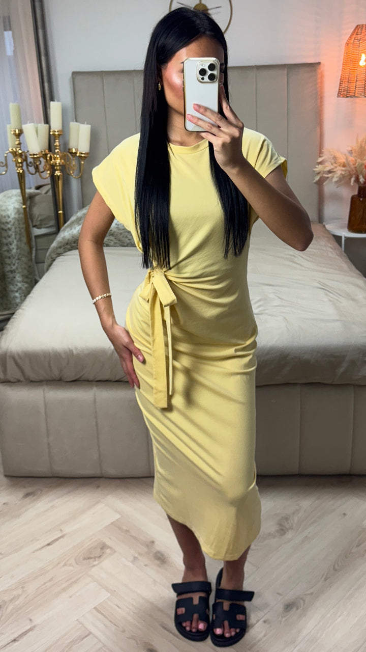 Front view of a model wearing the yellow Aurora midi dress with side bow detail and black sandals