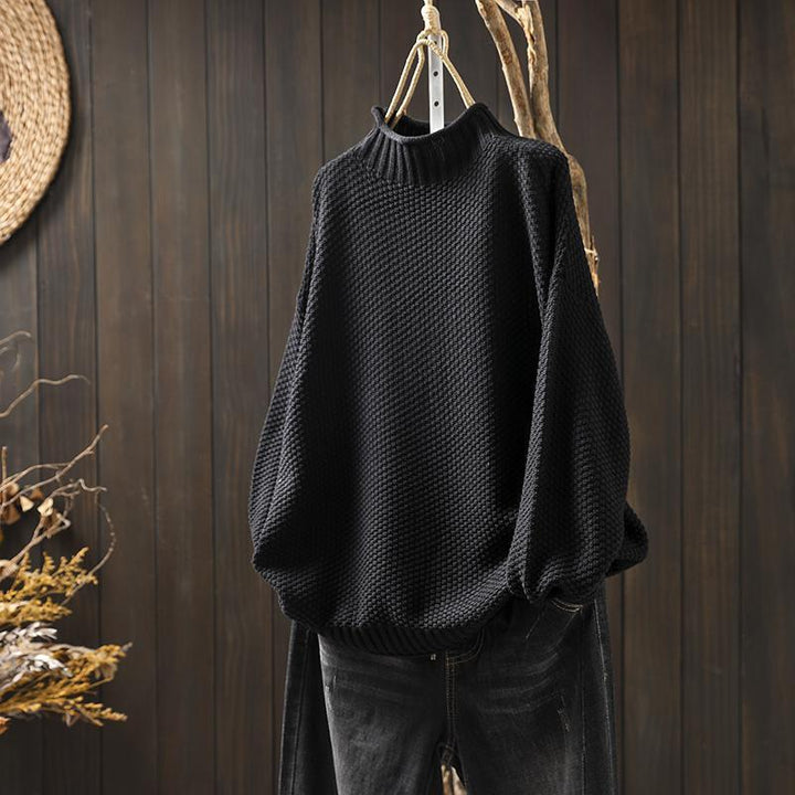 Front view of an oversized autumn pullover, a black textured knit sweater hanging on a branch with dark jeans