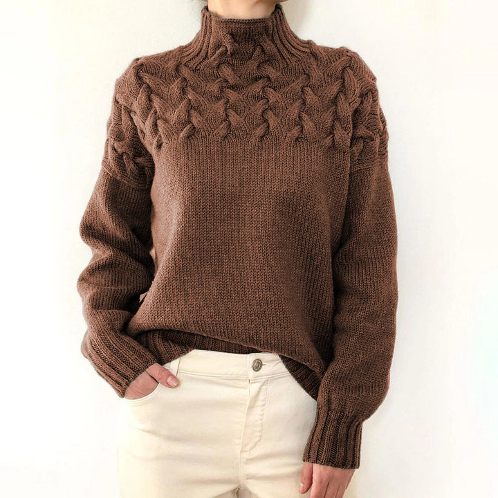 Front view of a model wearing a brown cable knit mock neck sweater with cream trousers, hand in pocket