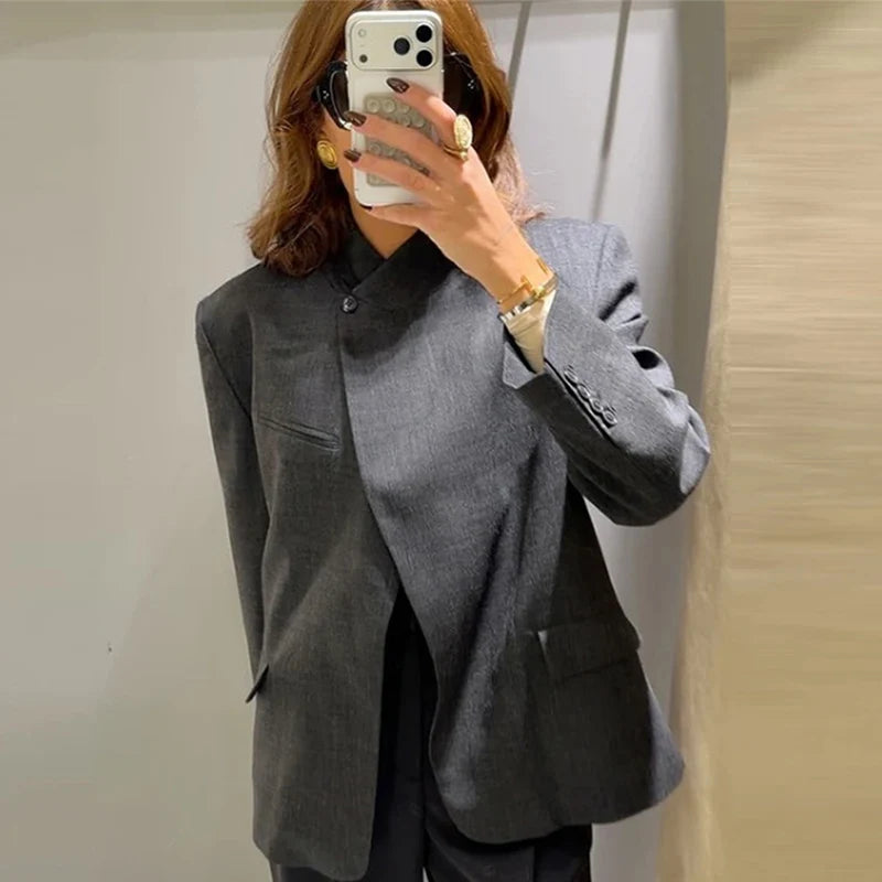 Worn by model, a charcoal grey collarless blazer with a single button closure and flap pockets