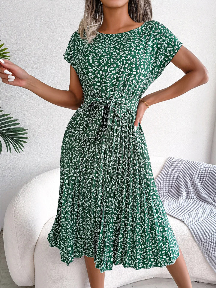 Front view of a model wearing a green floral pleated maxi dress with a tie waist and short sleeves