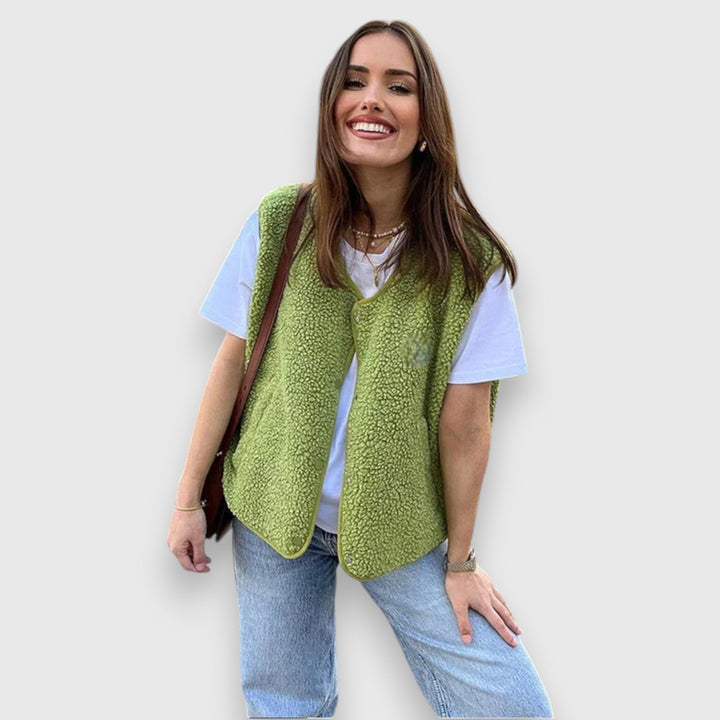 Front view, model smiling, wearing a green cosy fleece vest over a white tee and light blue jeans