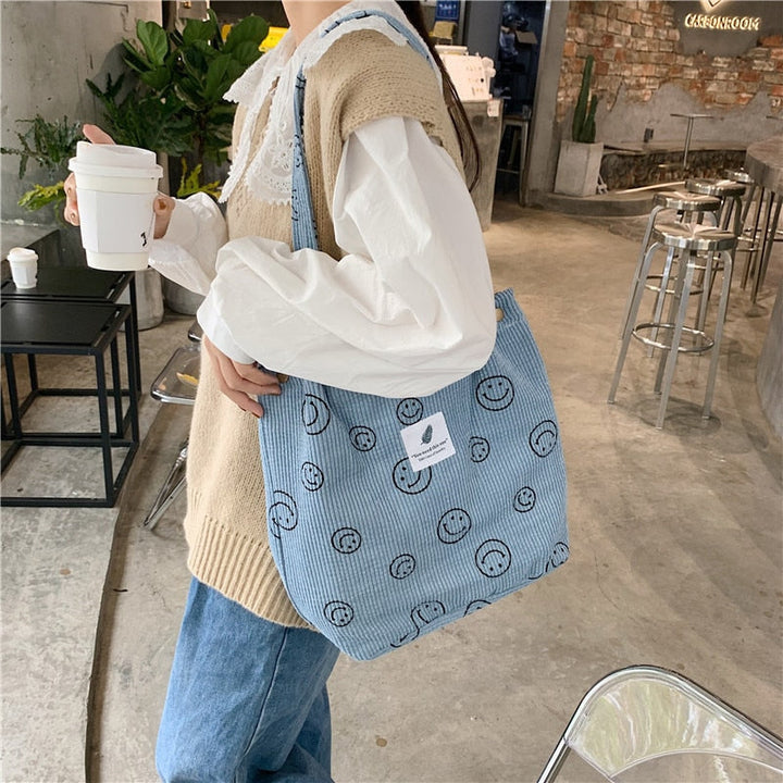 Light blue smiley print corduroy tote bag worn at her side