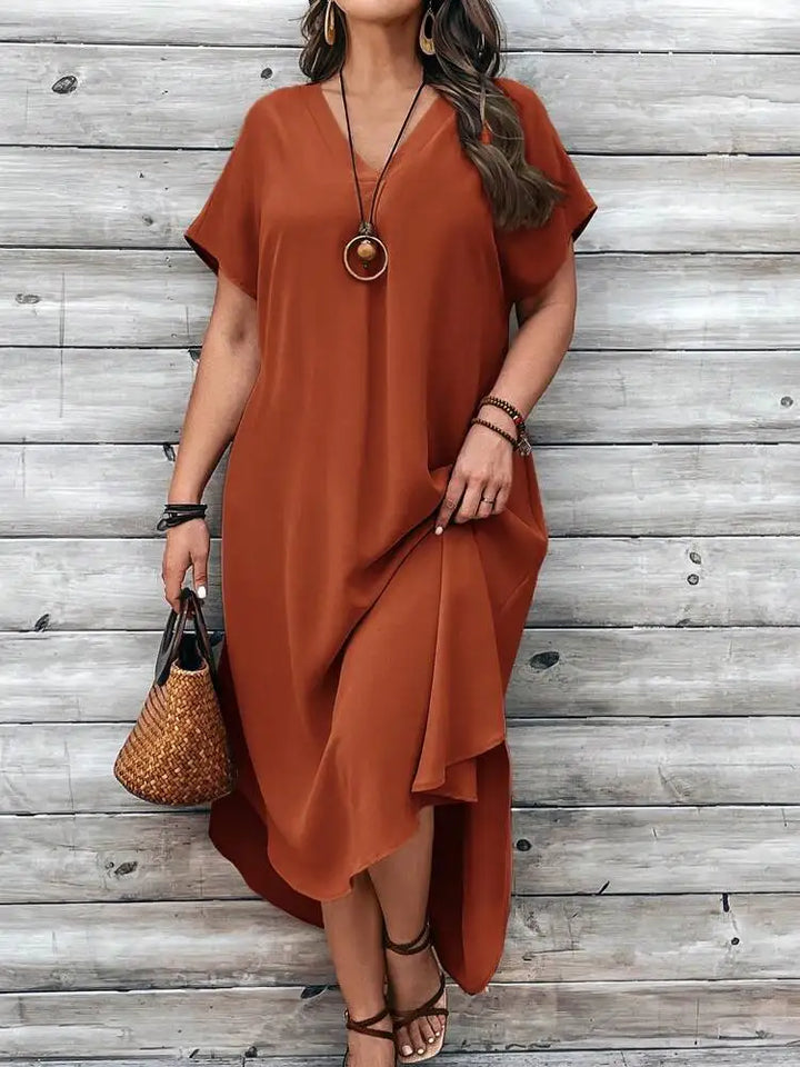Front view, worn by model, of a plus size V-neck casual dress in burnt orange with a long necklace and sandals