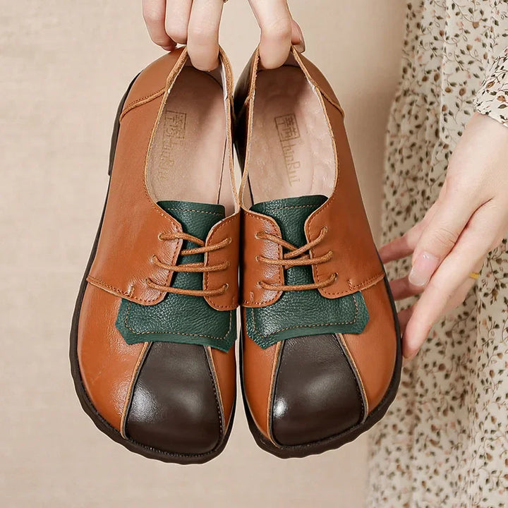Front view of Nora genuine leather flats, held by hands, showing brown, dark brown, and green panels