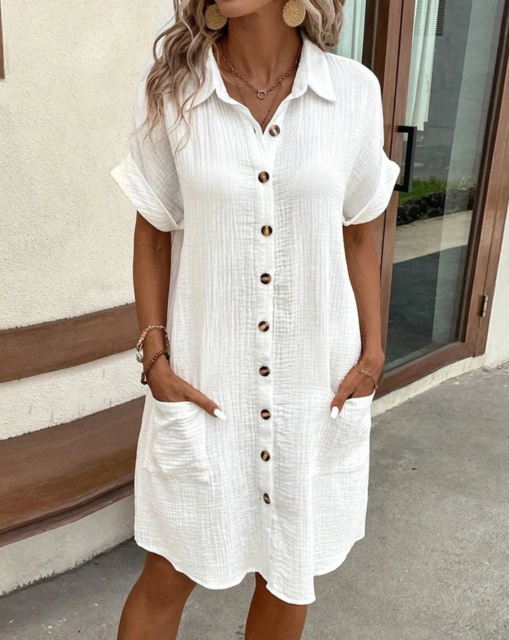 Front view of a model wearing a white cotton-linen mini dress with short cuffed sleeves and front pockets