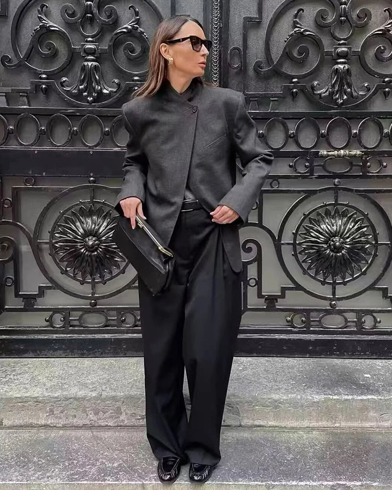 Worn by model, a charcoal grey collarless blazer with a mandarin collar and single button closure