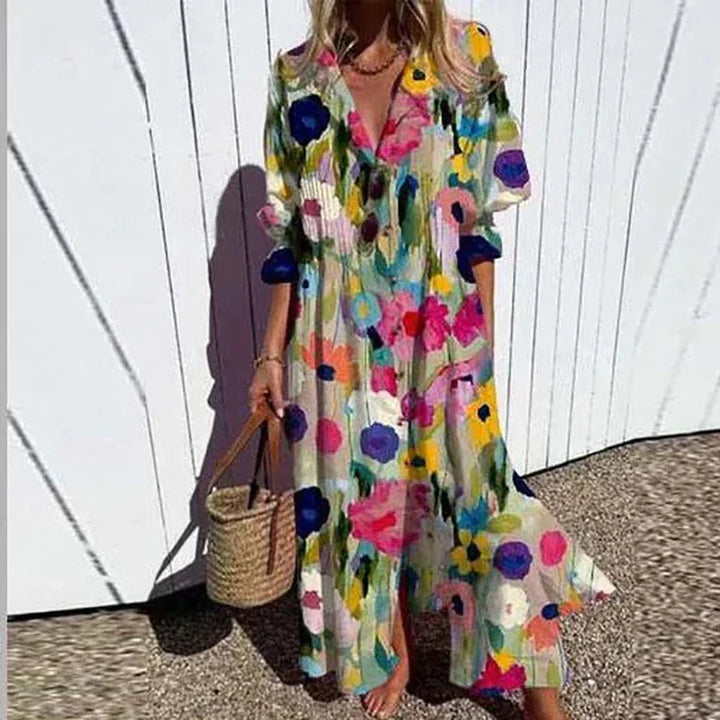 Front view of a model wearing the elegant pleated printed dress with a colourful floral pattern and a straw bag