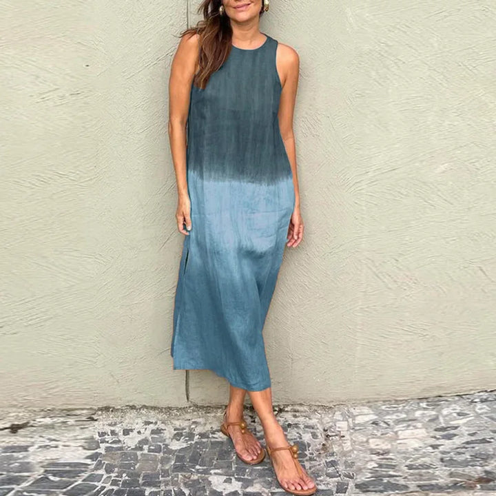 Front view of a model wearing a sleeveless ombre blue and green Boho print dress with side slits and sandals