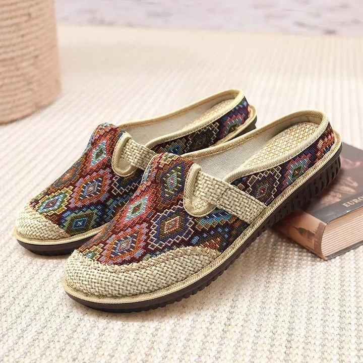 Front view of two ethnic linen slip-on shoes with colourful embroidered patterns and woven straw details