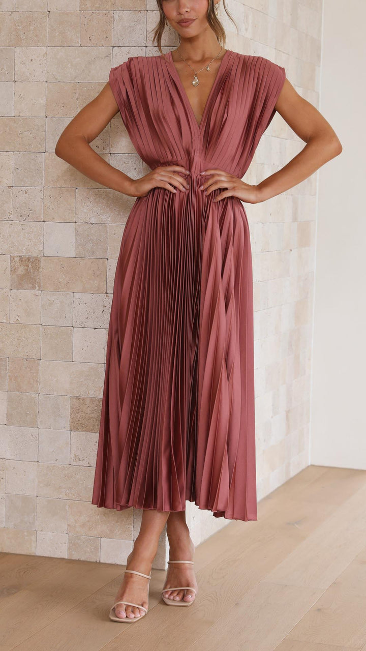 Front view of a model wearing an elegant pleated dress with a deep V-neck and high waist, hands on hips