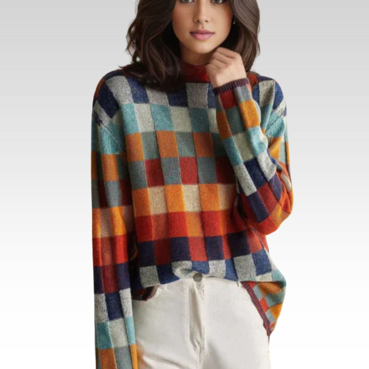 Front view, model wearing a colourful checkered knit jumper with high neck and white trousers