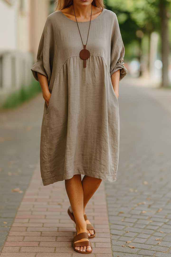 Front view of a model wearing a taupe round neck 3/4 sleeve boho dress with pockets and a brown necklace