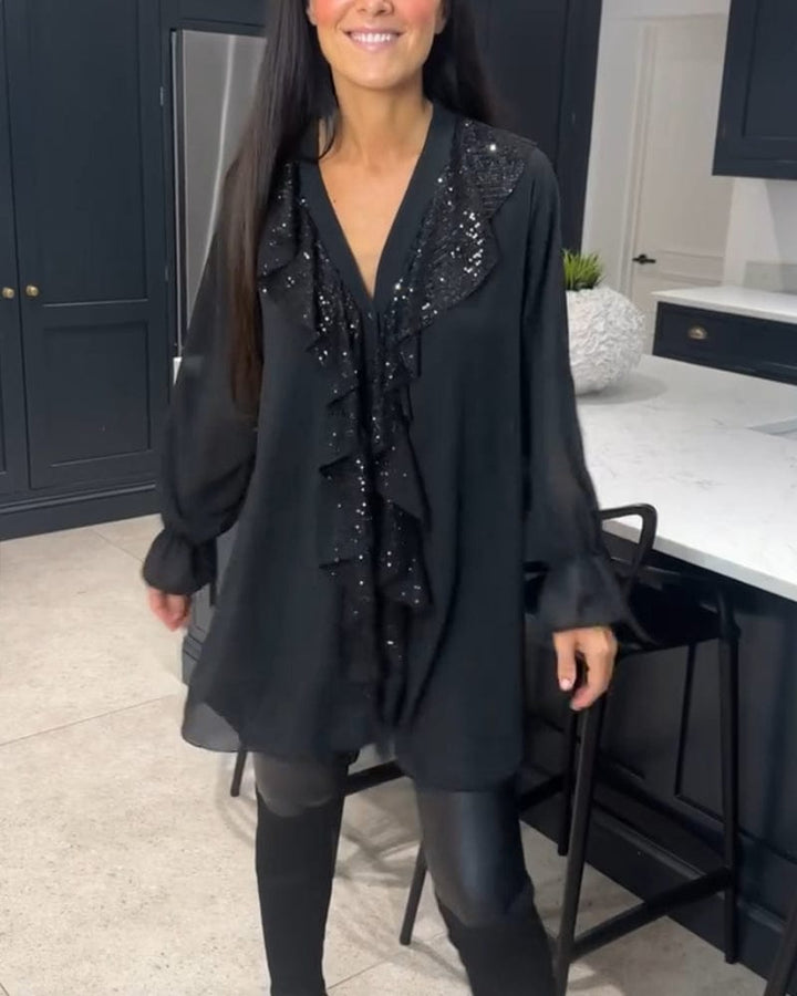 Front view of a woman wearing a black ruffled blouse with sequin detail over black pants