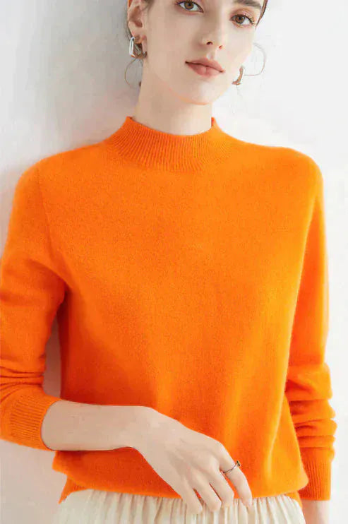 Front view, model wearing an orange cashmere mock-neck jumper with ribbed collar and cuffs, light pleated skirt