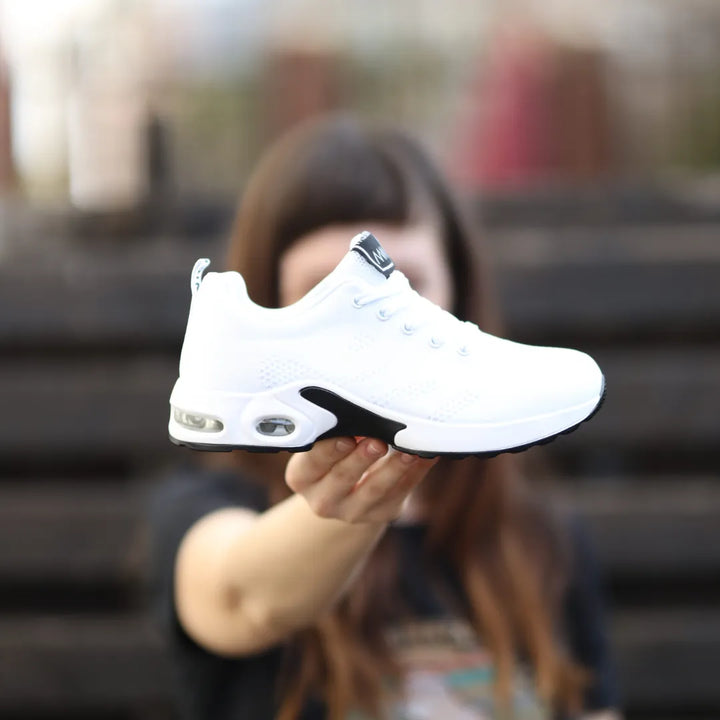 Side view, woman holding a white retro coloured pain-relieving sneaker with black accents and air cushion soles
