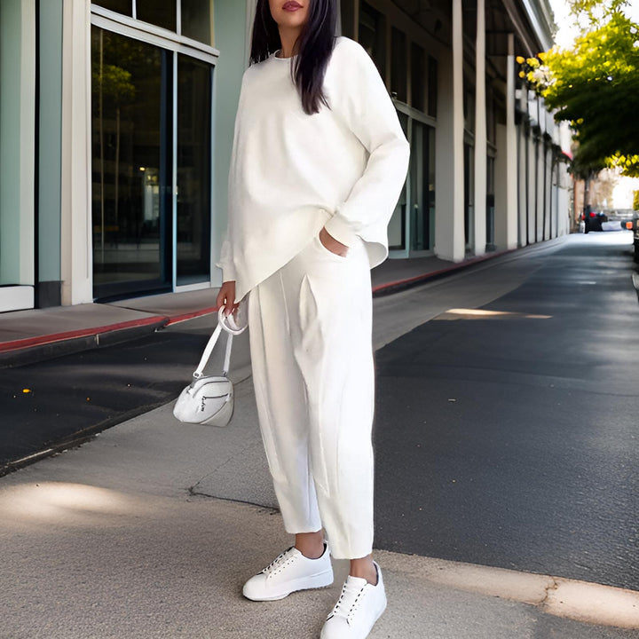 Front view, model wearing a white loose fit Elena Two-Piece Set, one hand in pocket, holding a small white bag