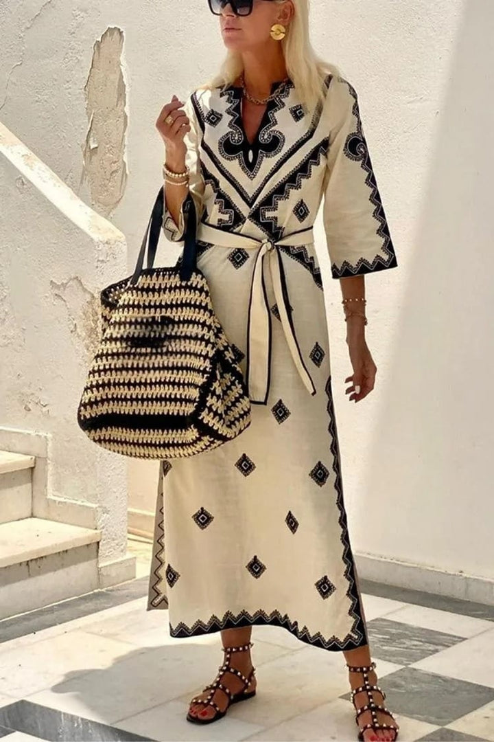 Front view of a model wearing a printed waist tie midi dress with black sandals and a woven bag