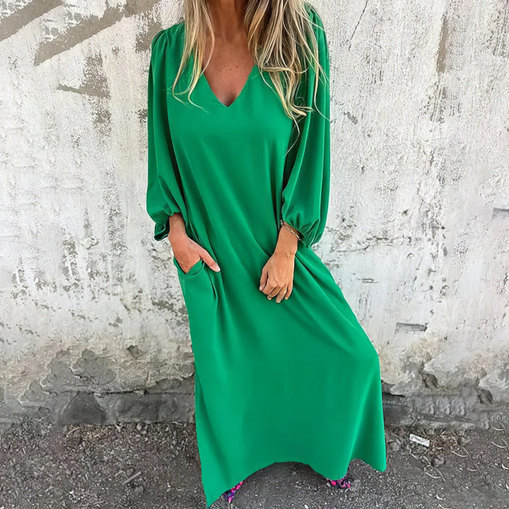 Front view of a woman wearing a green bohemian maxi dress with pockets, her hand in one pocket